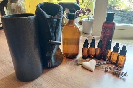 Glasflaschen mit ätherischen Ölen stehen auf dem Tisch mit Pflanzenölmischung, Lavendelblüten und einer 500 ml Braunglasflasche, einer Schutzhülle und Thermobecher.