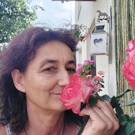 Marianne riecht an einer rosa-weissen Rose vor der Haustüre