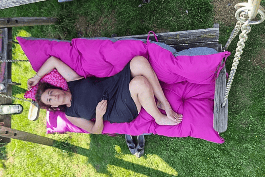 Marianne an ihrem Kraftplatz auf der alten Holzhängeschaukel zum Powernapping. Auf einem dicken pinkfarbenen Polster
