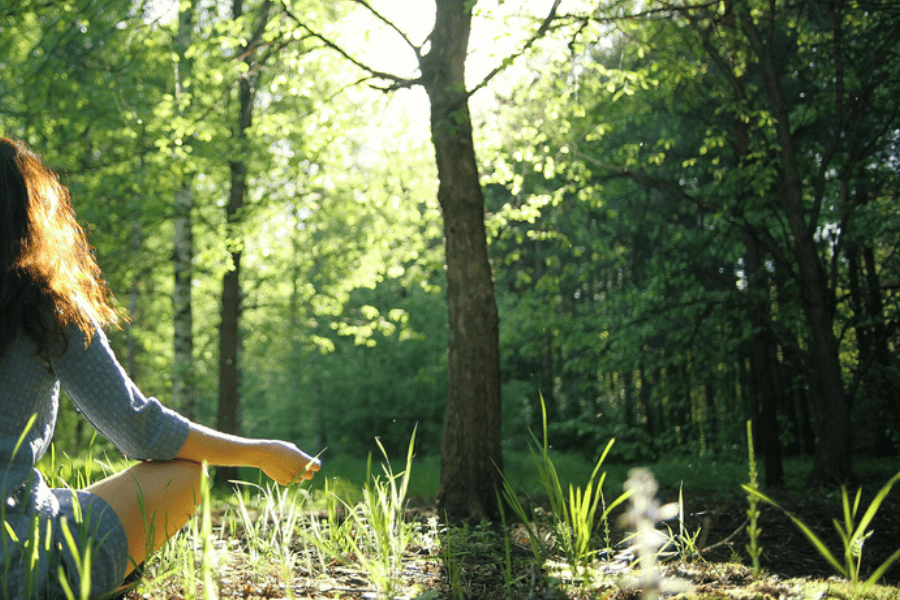 Frau sitzt am Waldboden in Meditationshaltung