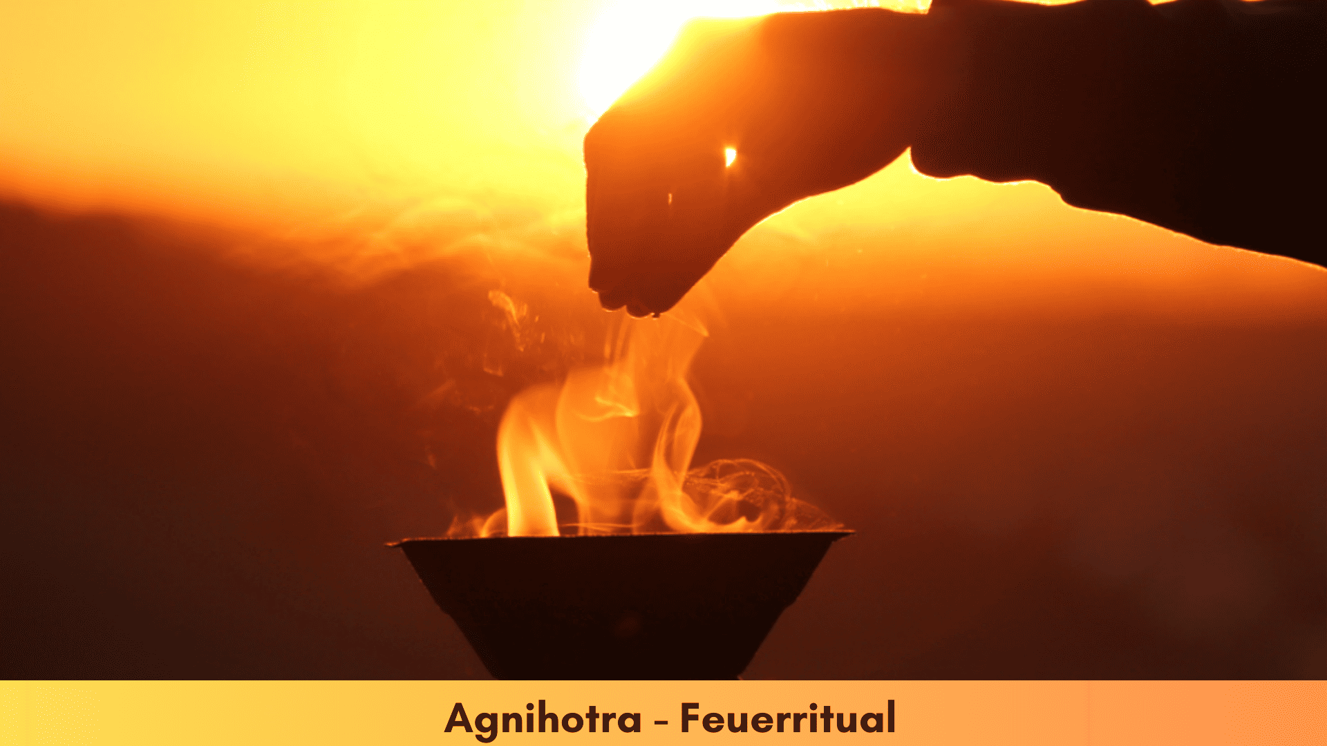 eine Agnihotra-Feuerschale bei Sonnenaufgang mit brennendem Feuer und eine Hand streut Reis darüber